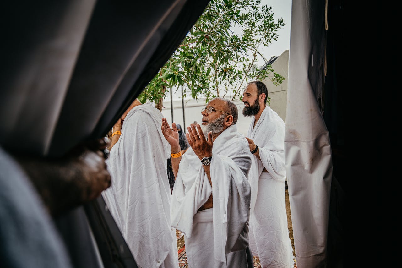 A group of men in white robes participate in a spiritual prayer outdoors, embracing cultural and religious traditions.