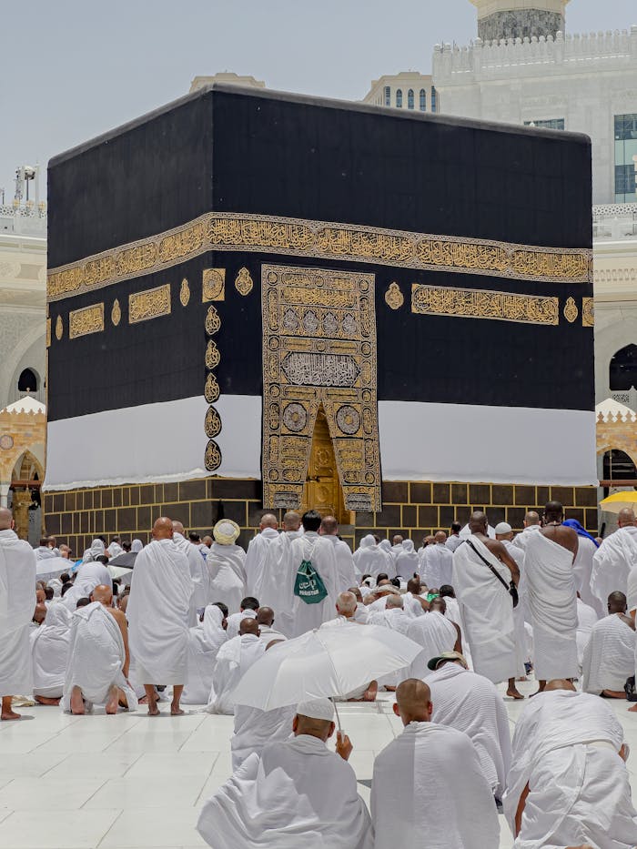 Pilgrims in white garments gather around the Kaaba in Mecca during daytime prayers.
